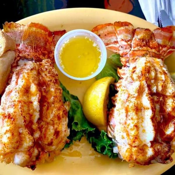 Two Keegan's Seafood Grille lobster tails with melted butter, lemon, and lettuce on a yellow plate.