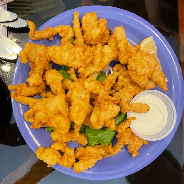 A blue plate filled with golden-brown fried clam strips, lettuce, a lemon wedge, and tartar sauce.